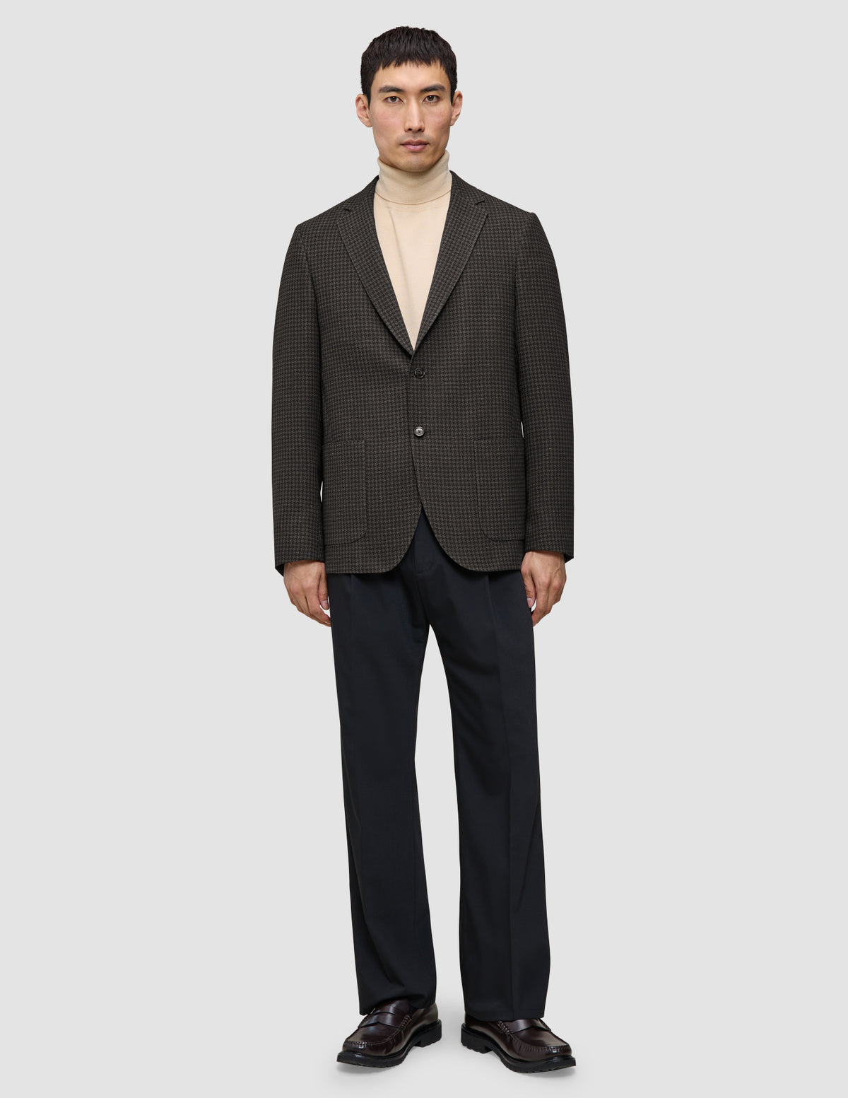 A person wearing a Timeless Wool Blazer Slim Dark Brown Check over a tan turtleneck and dark trousers.