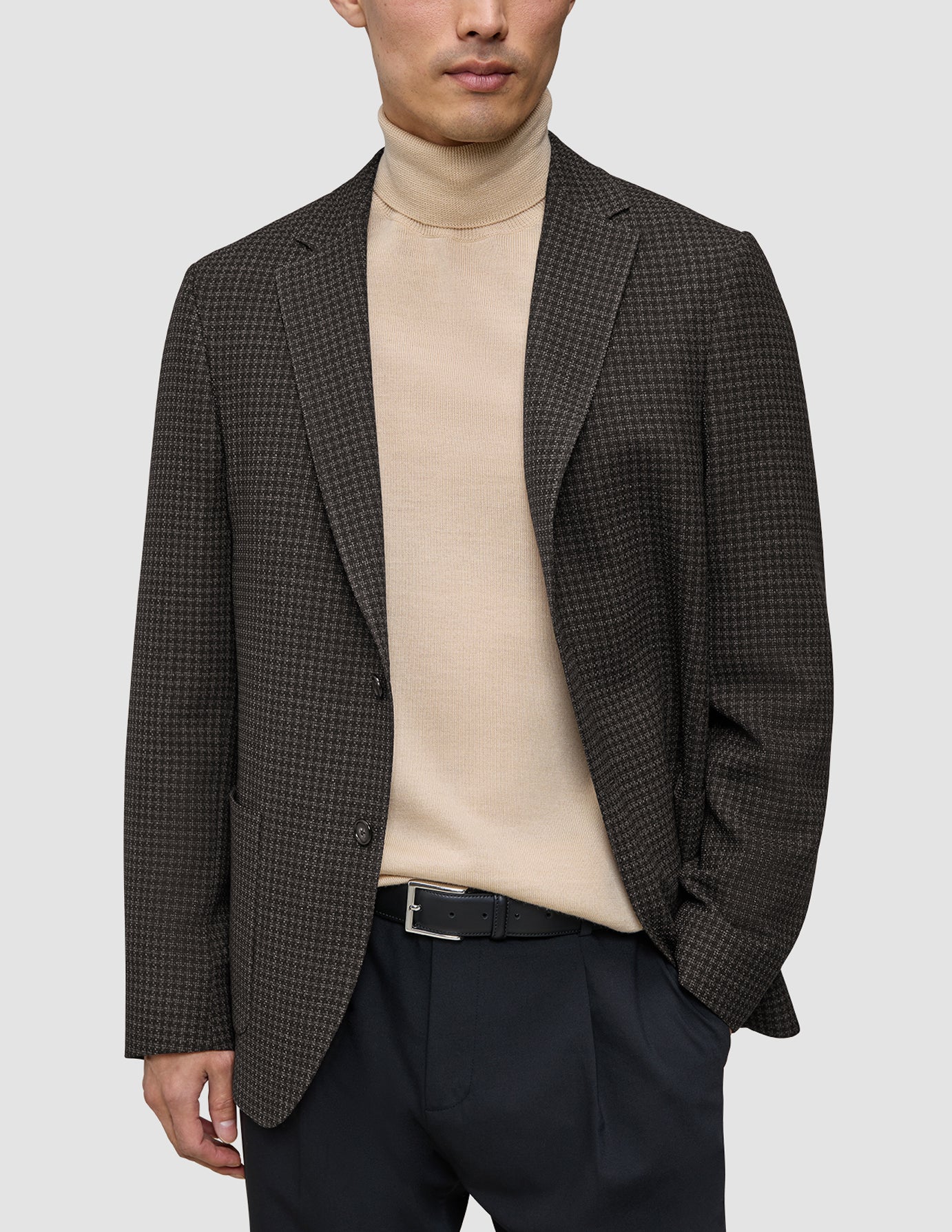 A person wearing a Timeless Wool Blazer Slim Dark Brown Check over a beige turtleneck sweater and black trousers.