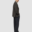 A man wearing a Timeless Wool Blazer Slim Dark Brown Check over a beige turtleneck sweater, paired with dark trousers and black loafers.