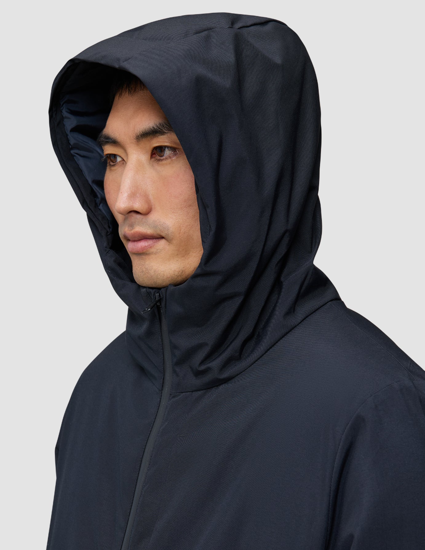 A person wearing a hooded black Utility Jacket Black with the hood pulled up over their head.
