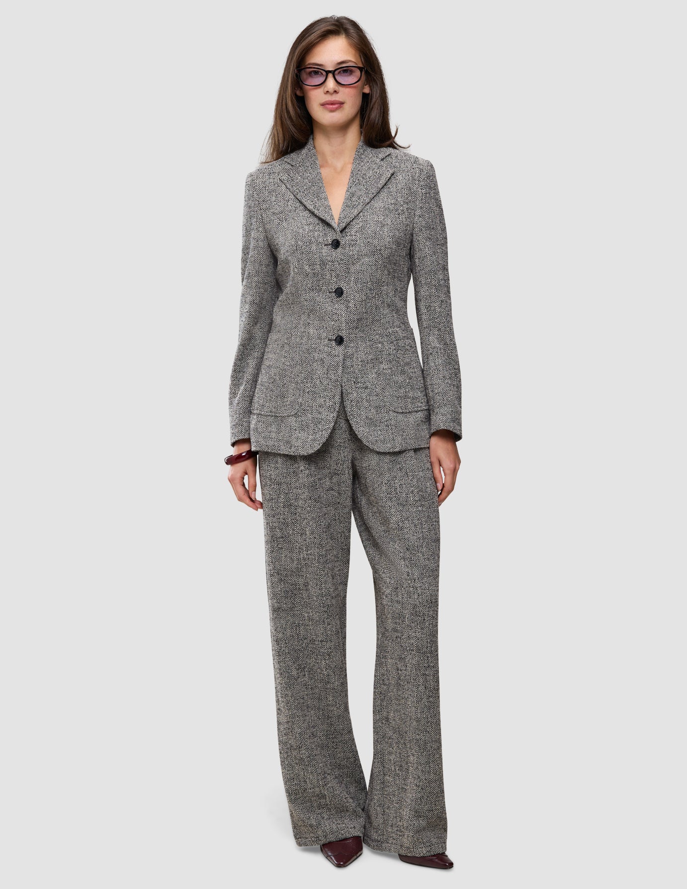 A model wearing a grey herringbone bouclé blazer with a three-button closure and matching Women Ashryn Pants Wide Domino Herringbone.