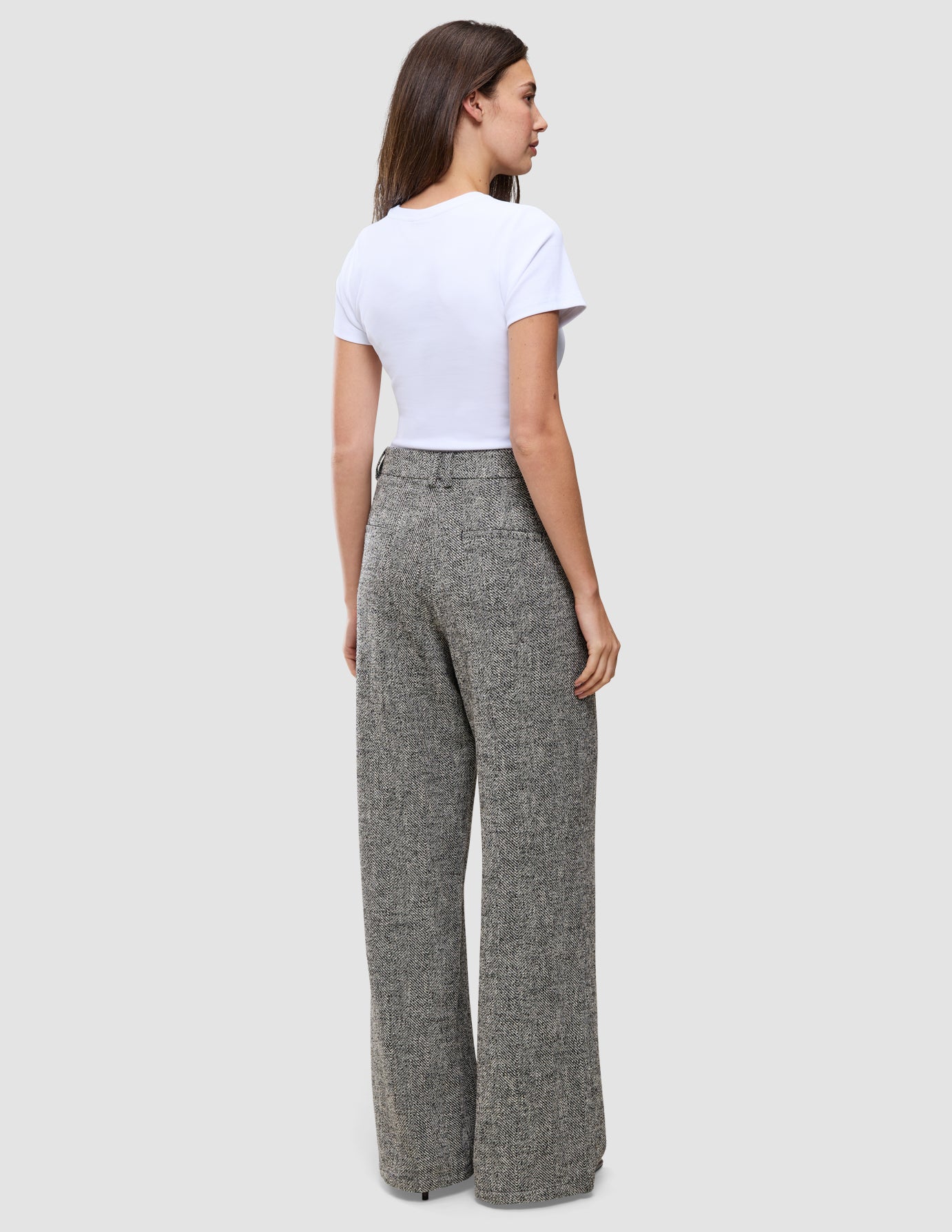 A woman seen from behind, wearing a white t-shirt and grey Women Ashryn Pants Wide Domino Herringbone with a high-waisted, wide-leg silhouette and a subtle herringbone bouclé texture.