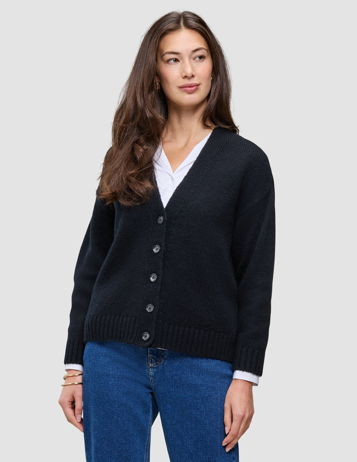 A person wears a Women Chunky Soft Wool Knit Cardigan Black over a white shirt and blue jeans.