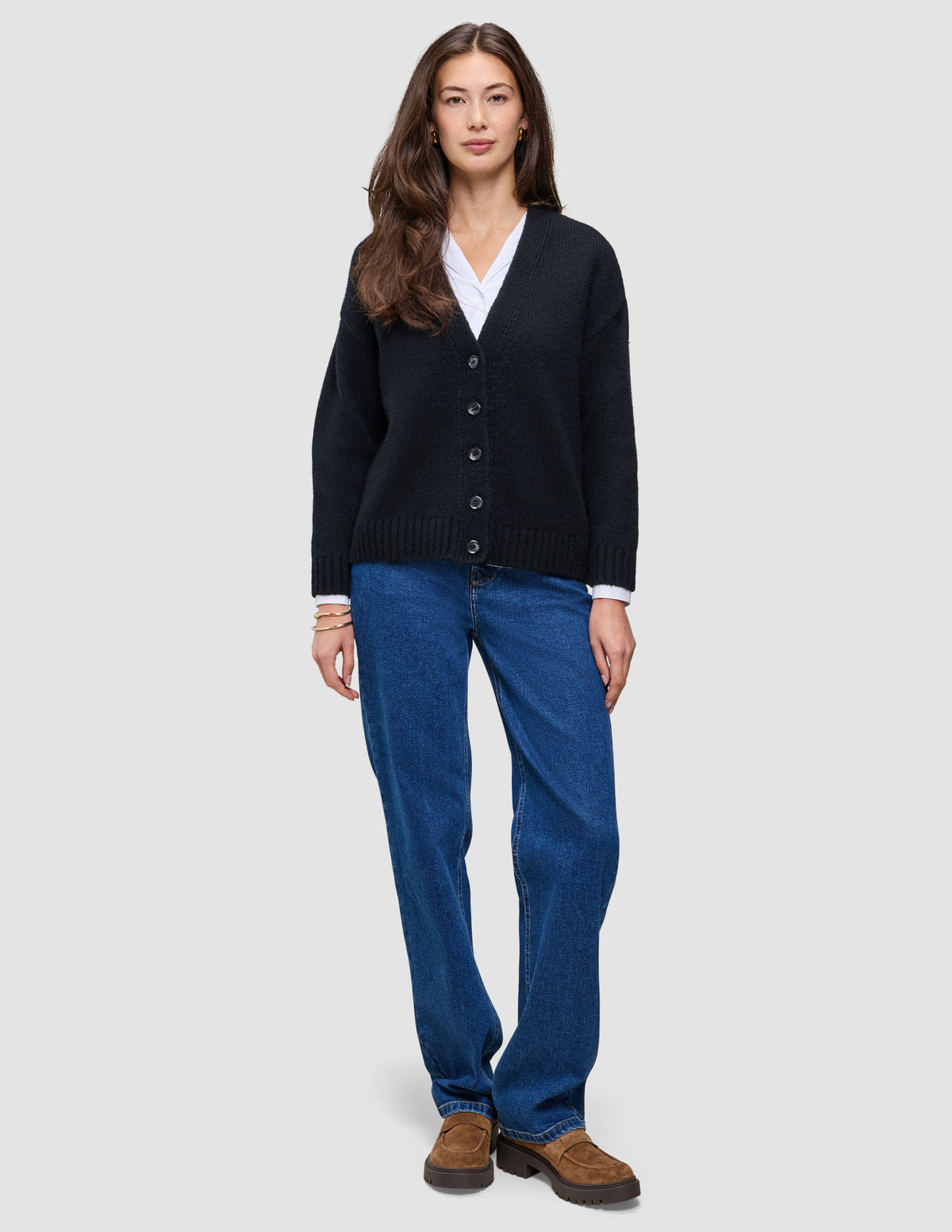 A woman wearing a Women Chunky Soft Wool Knit Cardigan Black over a white collared shirt, paired with blue jeans and brown loafers.