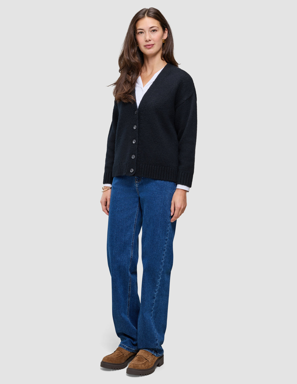 A woman wearing a Women Chunky Soft Wool Knit Cardigan Black over a white shirt, blue jeans, and brown loafers.