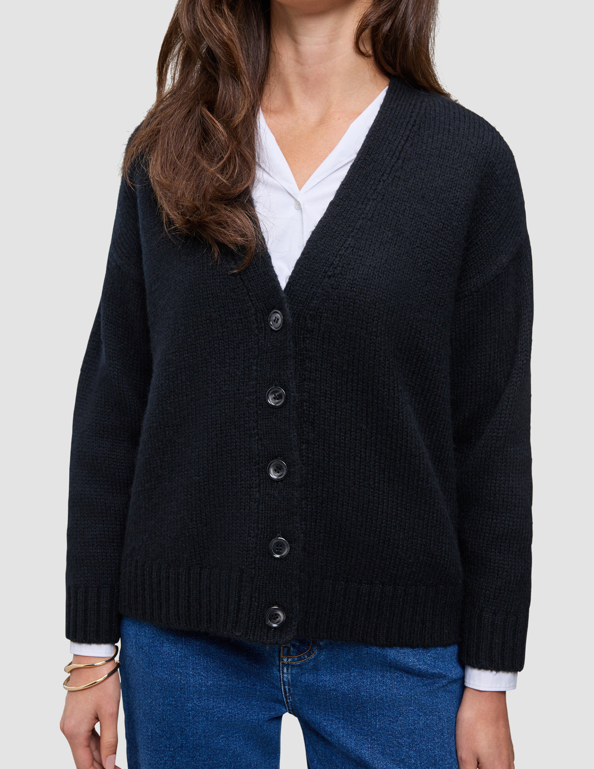 A cozy, chunky Women Chunky Soft Wool Knit Cardigan Black in a V-neck button-down style worn over a white shirt and blue jeans.