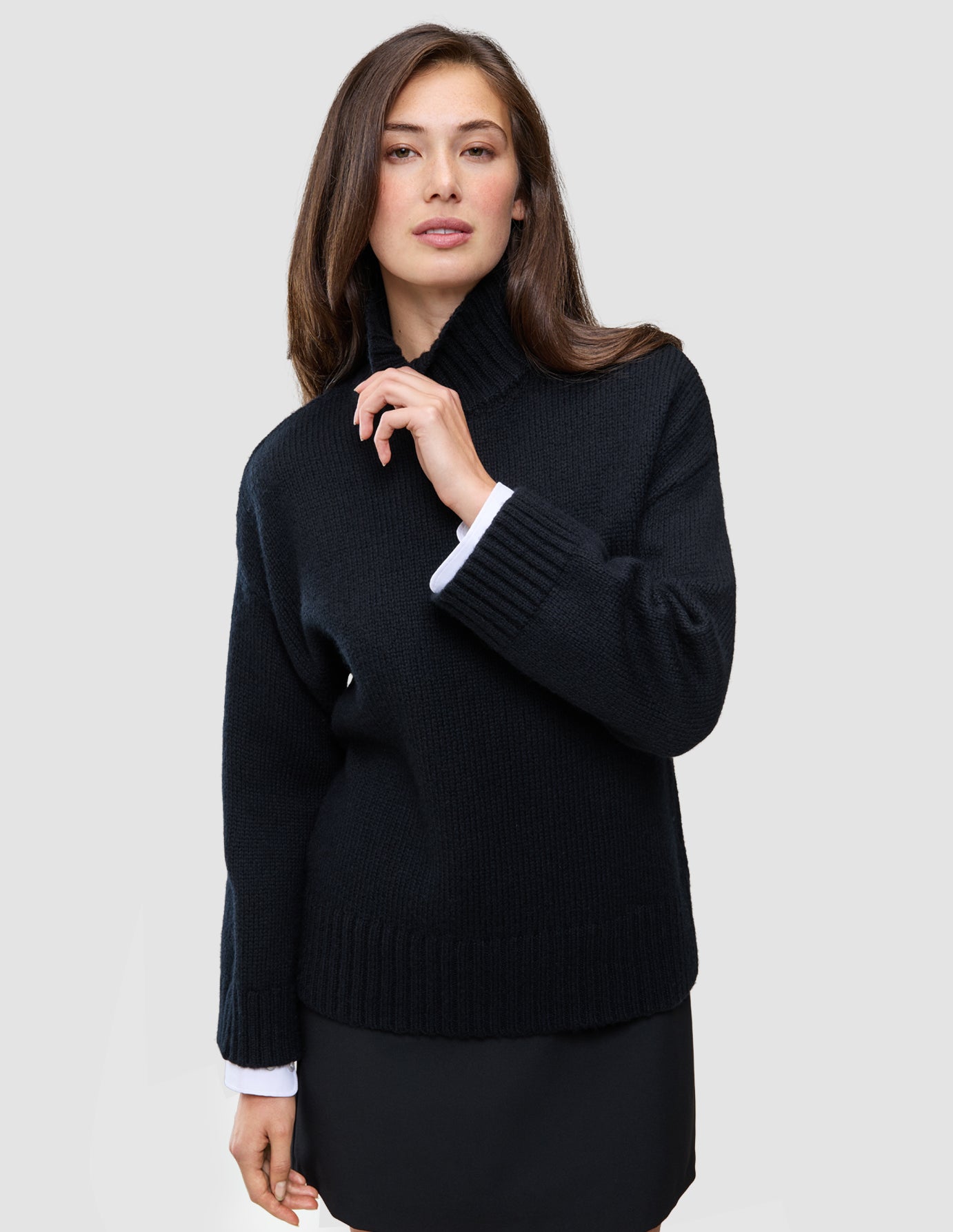 A person wears a Women Chunky Soft Wool Knit Turtleneck Black with white cuffs visible at the wrists, reflecting a clean Scandinavian design.