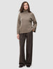 A person wearing a Women Chunky Soft Wool Knit Turtleneck Taupe Melange sweater and dark brown pinstriped trousers.