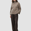 A woman wearing a Women Chunky Soft Wool Knit Turtleneck Taupe Melange in a Scandinavian design with dark brown pinstriped trousers.