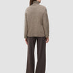 Seen from behind, a person wears the Women Chunky Soft Wool Knit Turtleneck Taupe Melange paired with dark brown pinstriped trousers, reflecting a minimalist Scandinavian design.