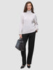 A woman wearing a beige turtleneck sweater and Women GO2 Pants Straight Black, holding a black handbag.
