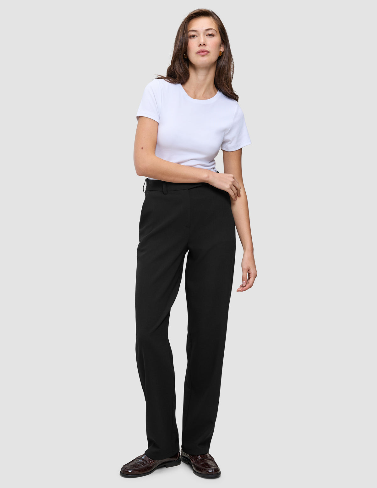 A woman wearing a white t-shirt, Women GO2 Pants Straight Black, and dark loafers.
