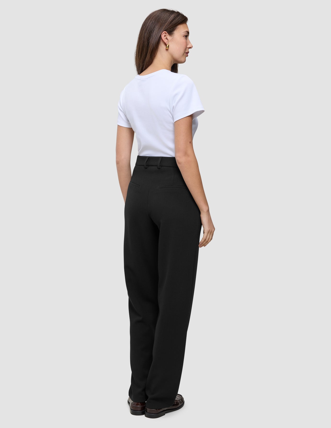 A person seen from behind wears a white t-shirt tucked into Women GO2 Pants Straight Black, embodying a minimalist Scandinavian design aesthetic.