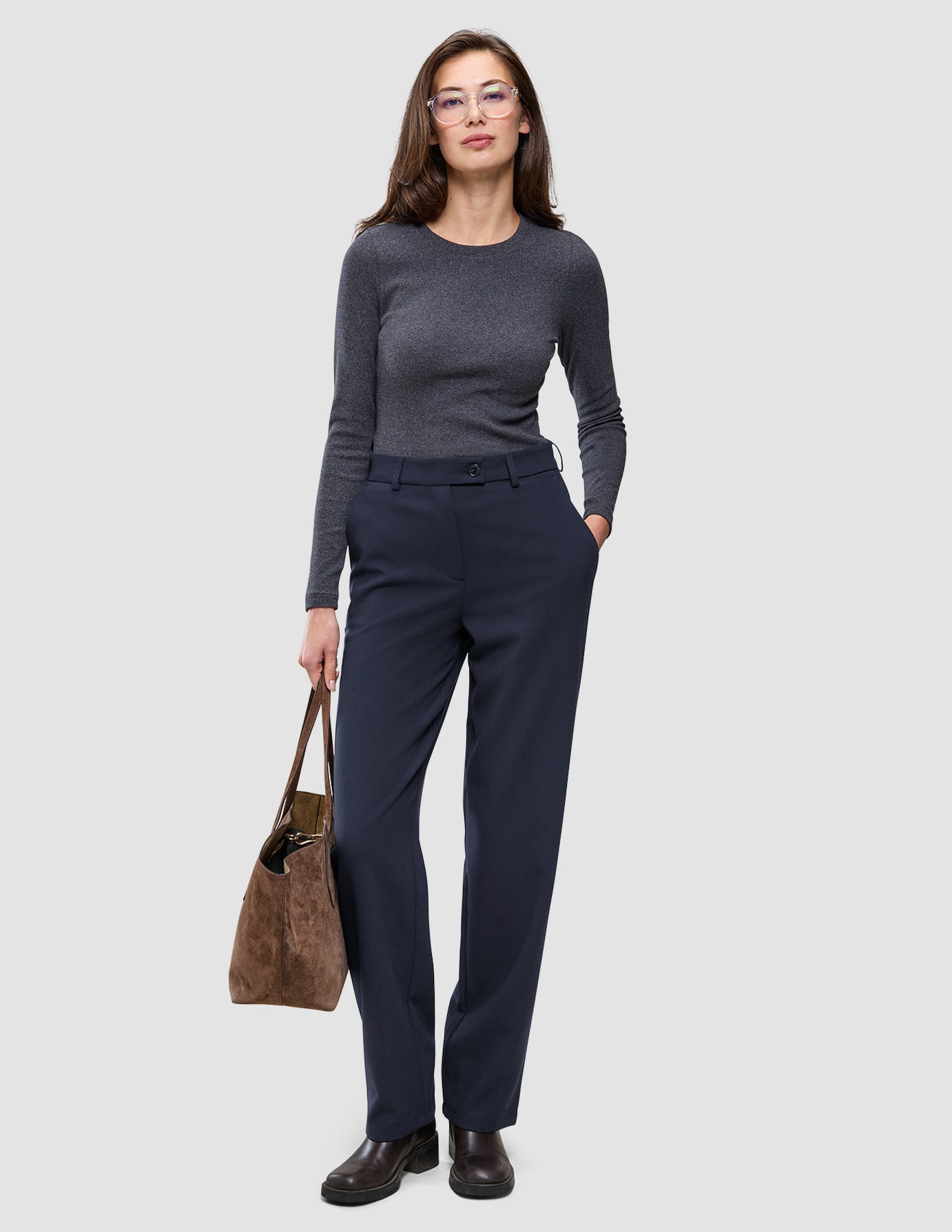 A woman wearing a gray long-sleeved shirt and Women GO2 Pants Straight Blue Nights, holding a brown handbag.