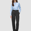 A woman wearing a light blue button-down shirt tucked into Women GO2 Pants Straight Dark Grey Melange with a black belt and black shoes.