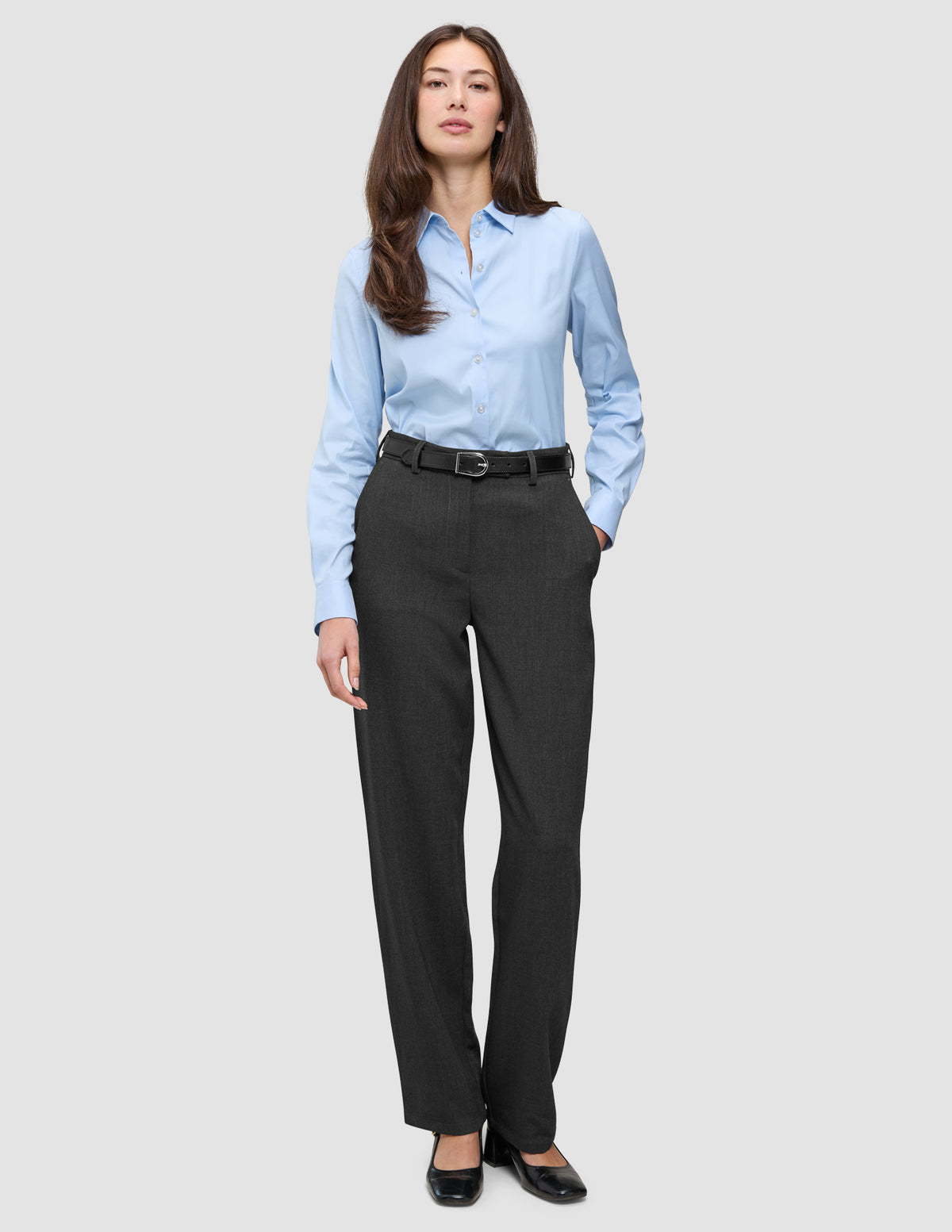 A woman wearing a light blue button-down shirt tucked into Women GO2 Pants Straight Dark Grey Melange with a black belt and black shoes.