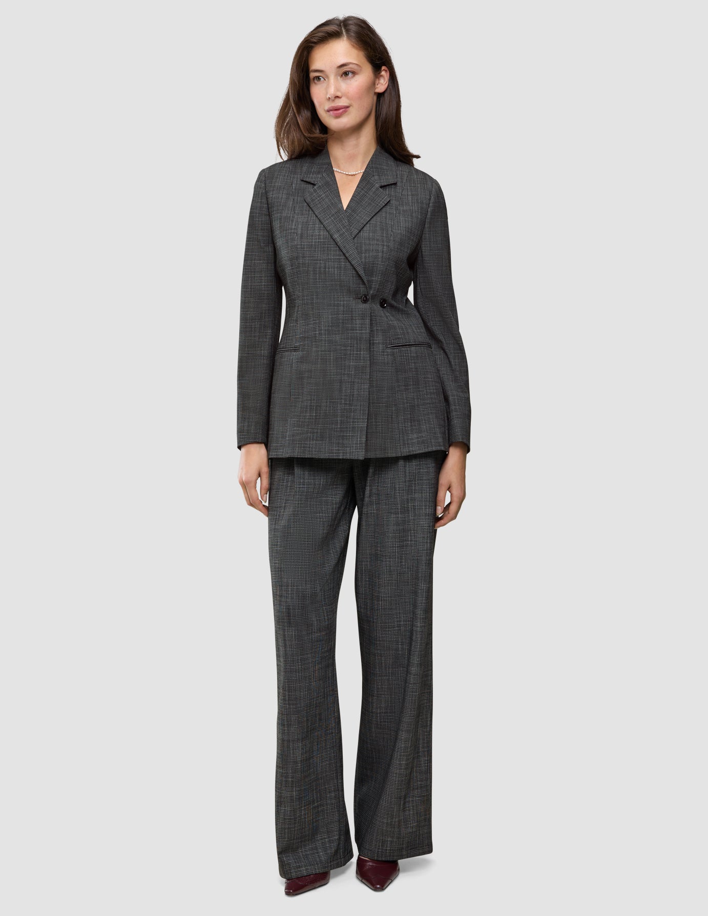A woman wearing the Women Nara Blazer Fitted Black Check in charcoal gray plaid, paired with matching wide-leg trousers in a Scandinavian design.