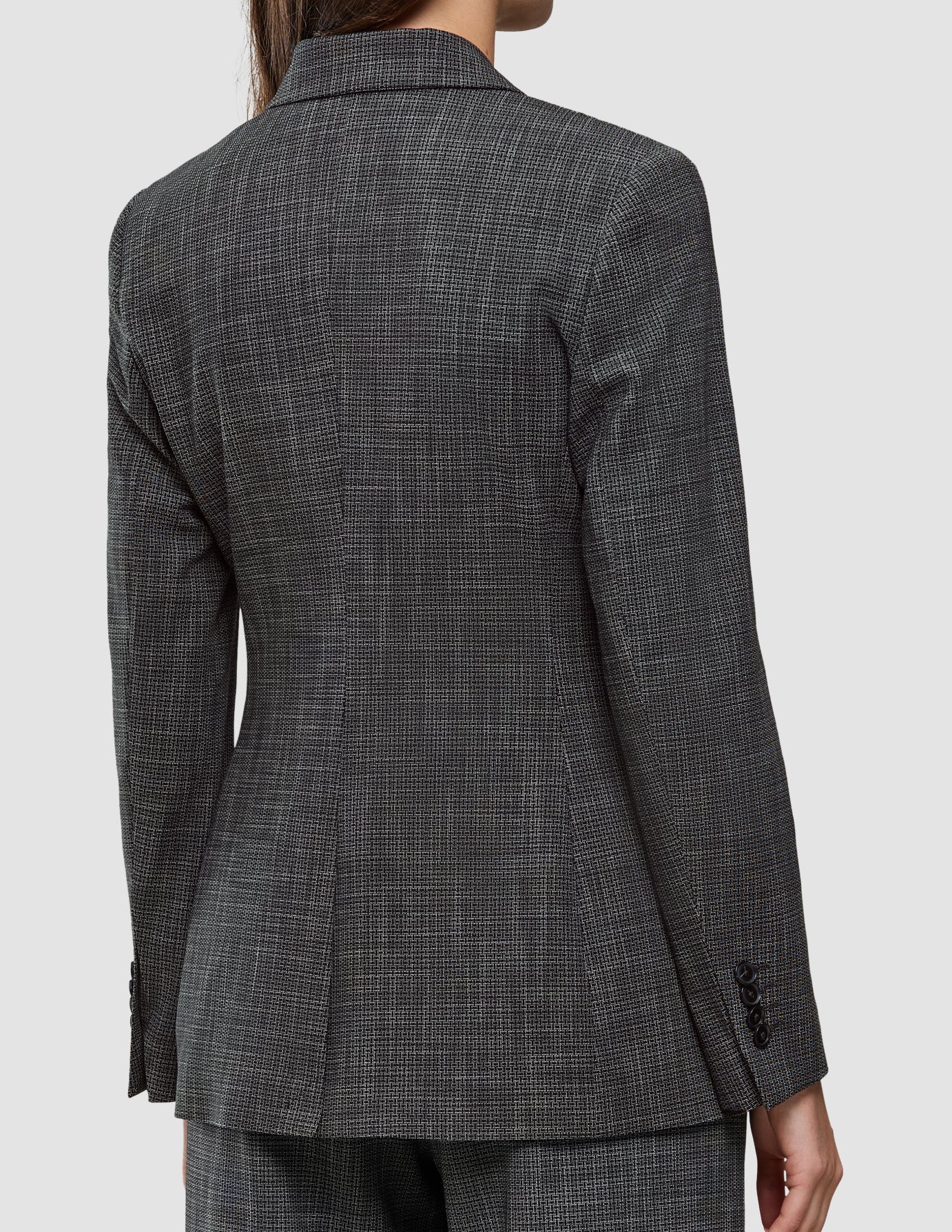 Back view of a person wearing a Women Nara Blazer Fitted Black Check, featuring a tailored black and white check design with notched lapels and buttoned cuffs.