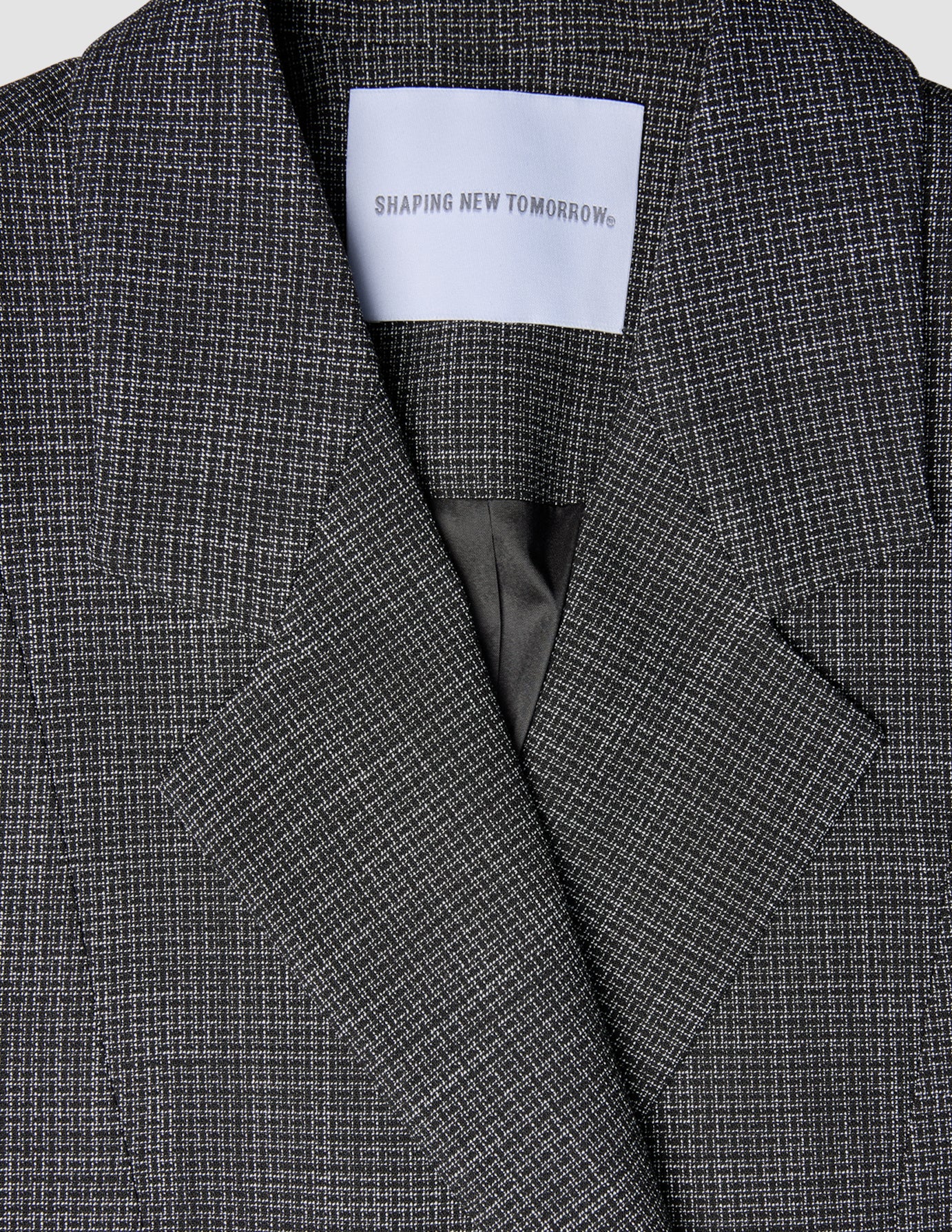 Close-up of a Women Nara Blazer Fitted Black Check, featuring a black and white micro-check pattern and a brand label at the collar.