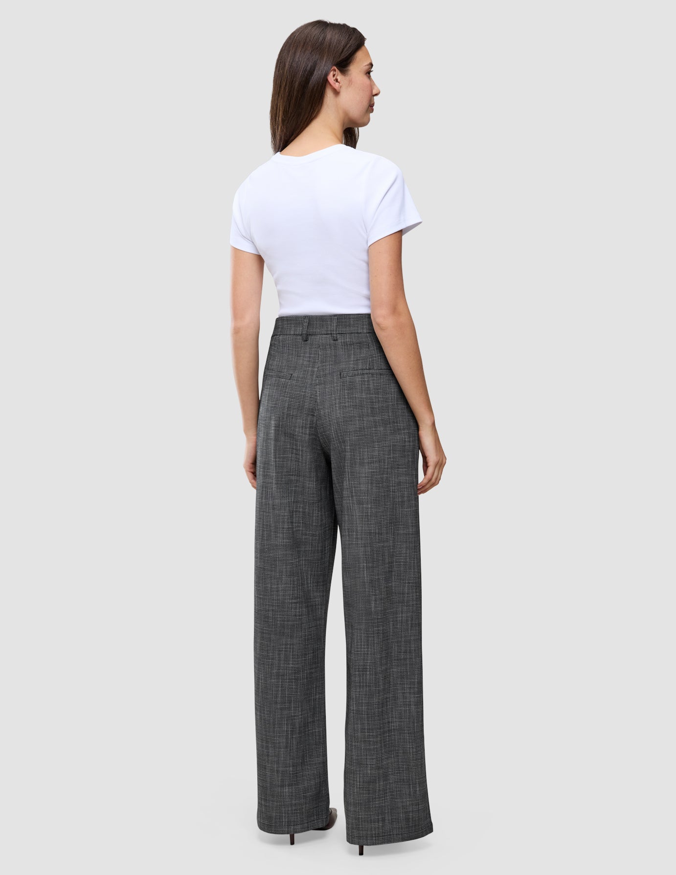 A person seen from behind wearing a white t-shirt and high-waisted Women Nara Pants Wide Black Check in a gray checkered print.