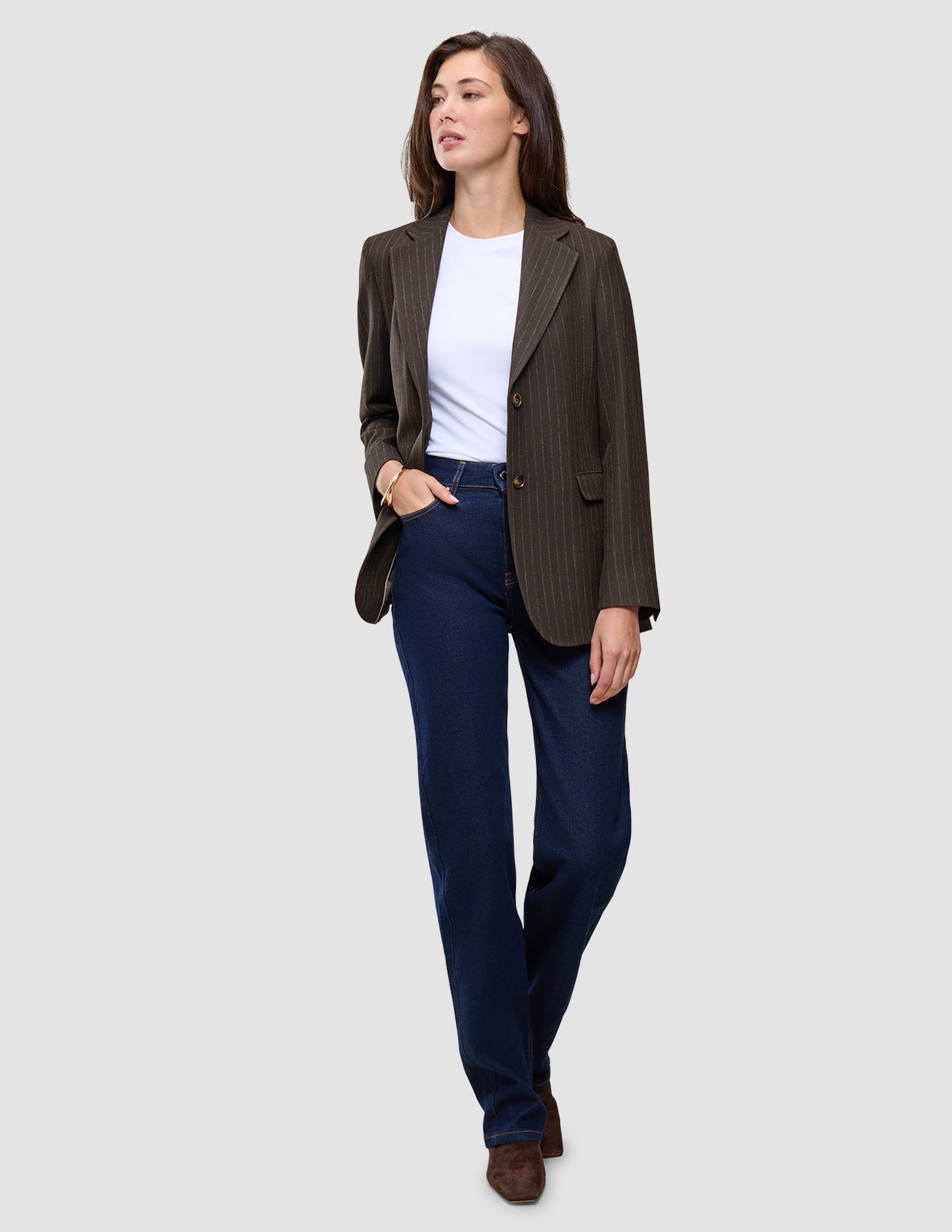 A woman wearing a Women Serene Blazer Regular Walnut Herringbone, white t-shirt, and dark blue jeans.