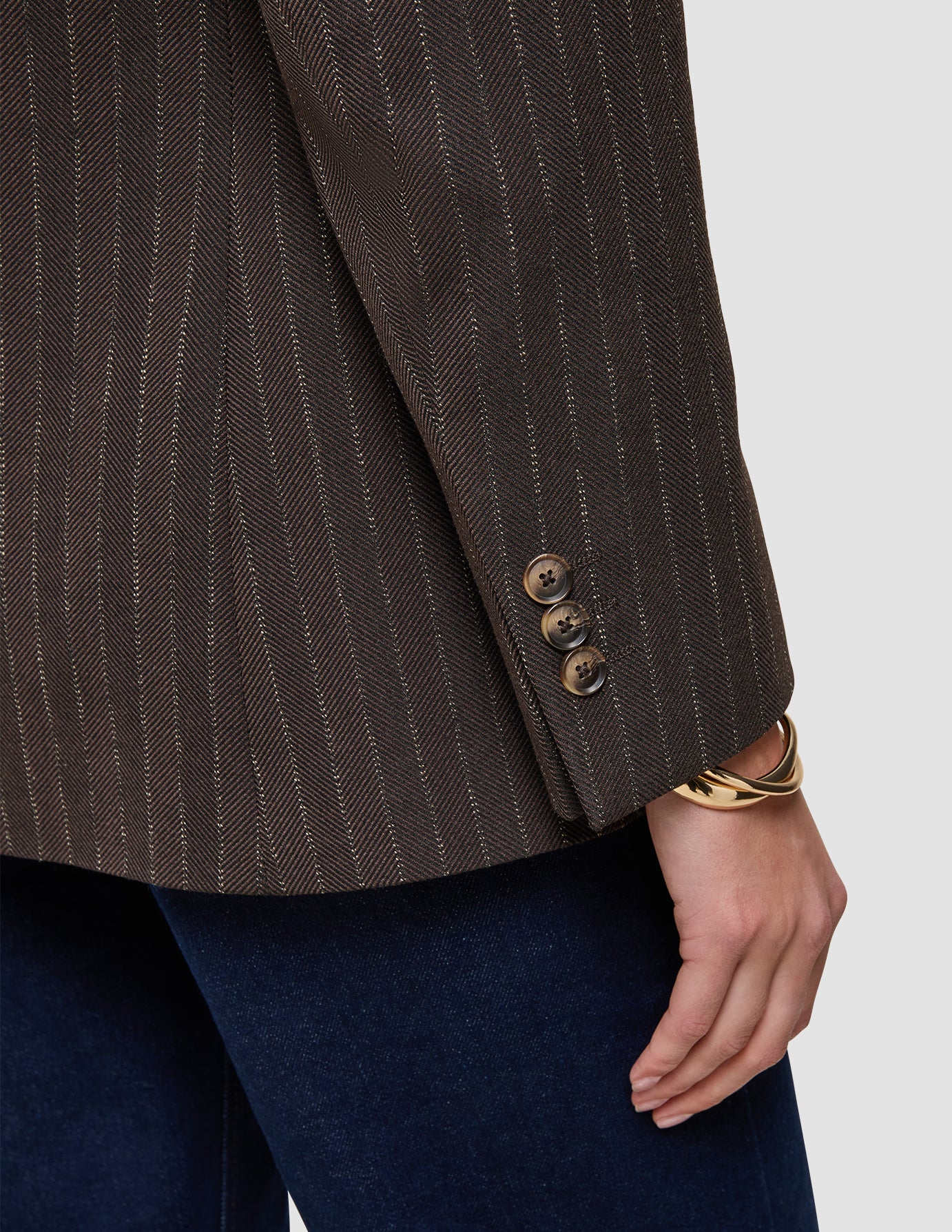 Close-up of a brown Women Serene Blazer Regular Walnut Herringbone featuring three buttons on the sleeve cuff, worn with dark denim jeans.