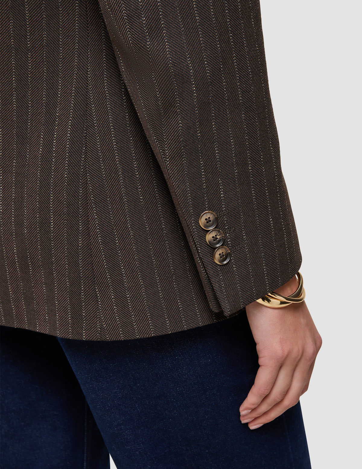 Close-up of a brown Women Serene Blazer Regular Walnut Herringbone featuring three buttons on the sleeve cuff, worn with dark denim jeans.