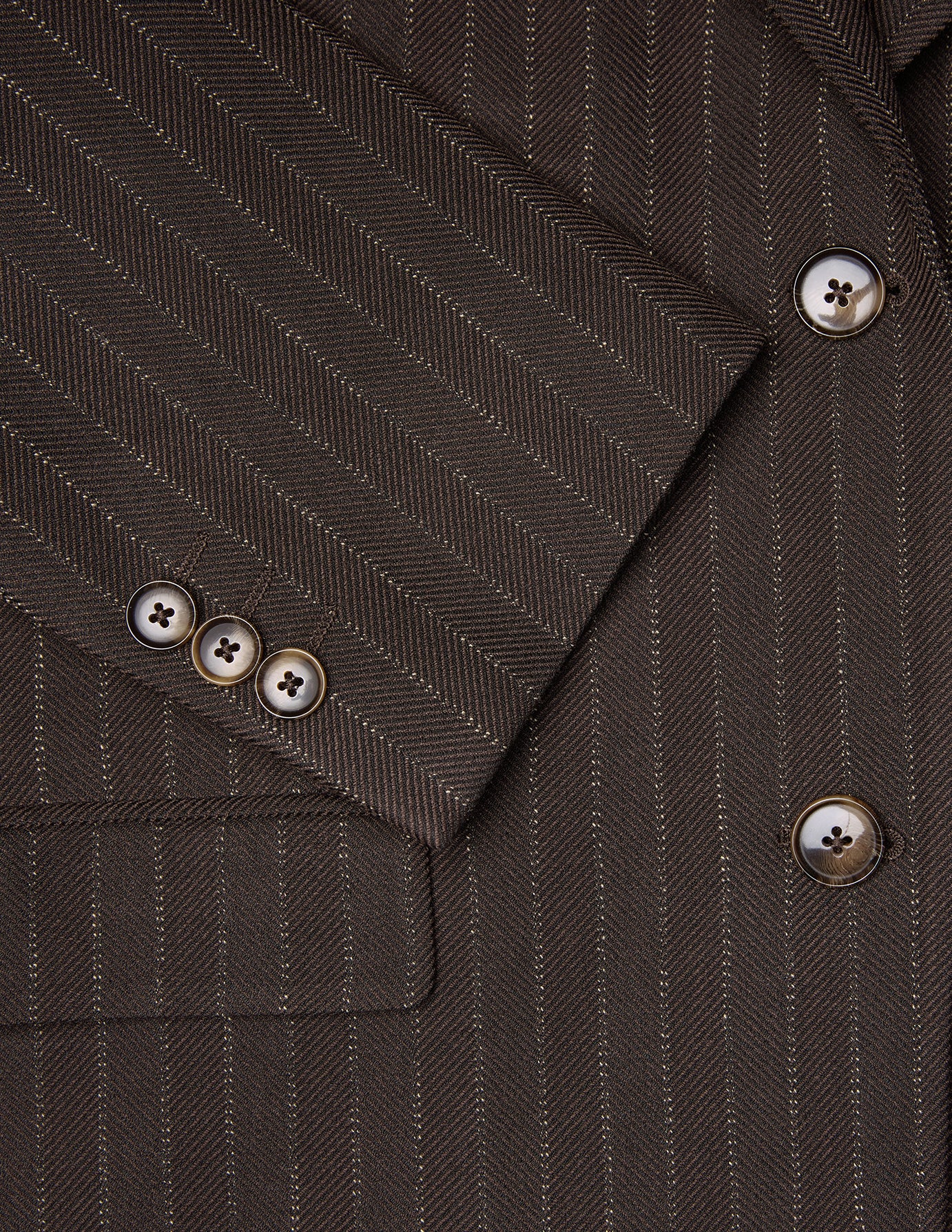 Close-up of a Women Serene Blazer Regular Walnut Herringbone featuring a brown herringbone wool pattern with vertical pinstripes and tortoiseshell buttons on the cuff and front.