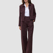 A woman wears a dark pinstriped Women Serene Pants Wide Berry Pinstripe blazer and matching wool-like wide-leg trousers over a white collared shirt.