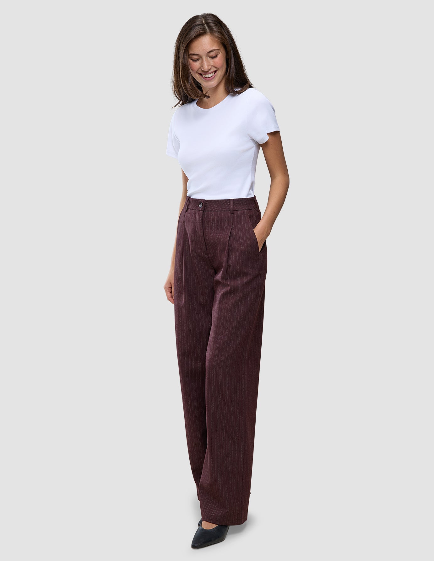 A woman wears a white t-shirt and Women Serene Pants Wide Berry Pinstripe in a Scandinavian design.