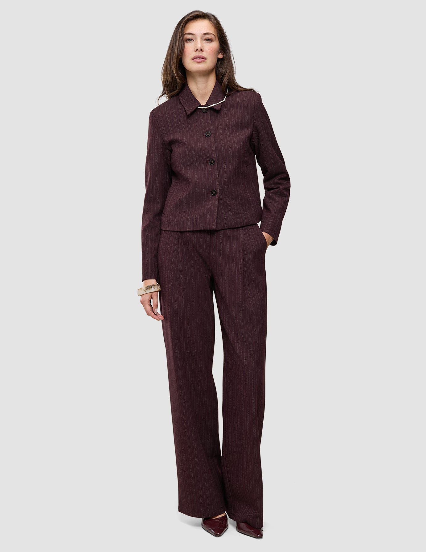 A woman wearing a Women Serene Short Jacket Berry Pinstripe and matching trousers in a dark berry pinstripe fabric with Scandinavian design elements.