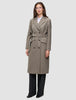 A woman wears a Women Wool Coat Greige, a long, double-breasted grey-brown wool coat with a matching tie belt over a white shirt and black trousers, showcasing minimalist Scandinavian design.