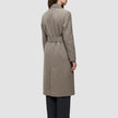 A person viewed from the back wearing a Women Wool Coat Greige, a long, double-breasted wool coat with a belted waist over dark trousers.